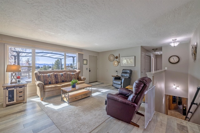 living room featuring a textured ceiling, light wood-style flooring, and baseboards