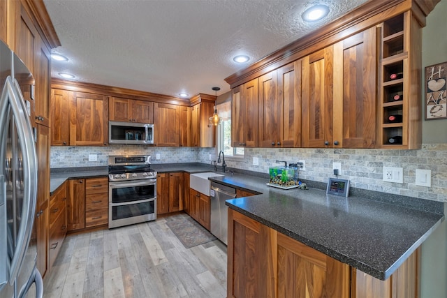 kitchen featuring light wood finished floors, brown cabinetry, appliances with stainless steel finishes, a peninsula, and a sink