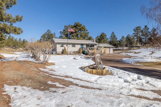 snow covered house with a garage, a chimney, and an outdoor structure