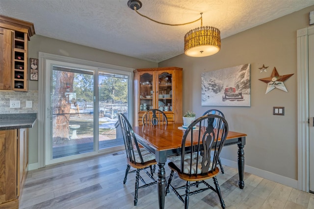 dining area featuring light wood-style flooring, visible vents, baseboards, and a textured ceiling