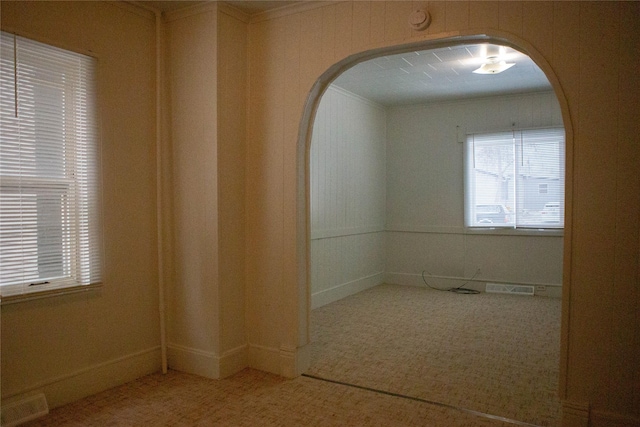 carpeted empty room with arched walkways, ornamental molding, and visible vents