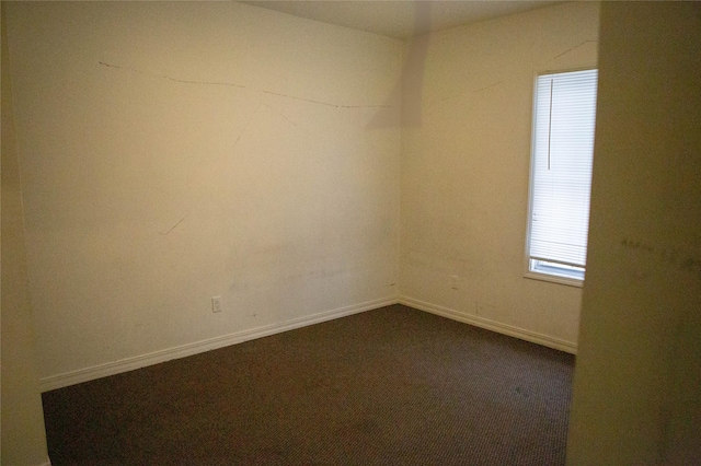 unfurnished room featuring dark colored carpet and baseboards