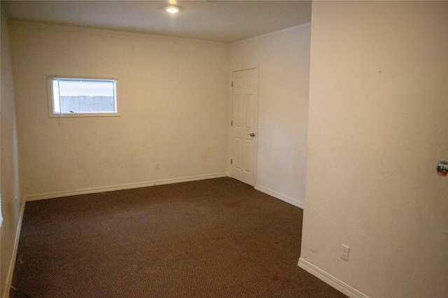 spare room with baseboards, dark colored carpet, and crown molding