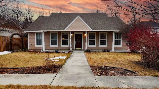 view of front of home featuring a yard, covered porch, fence, and a shingled roof