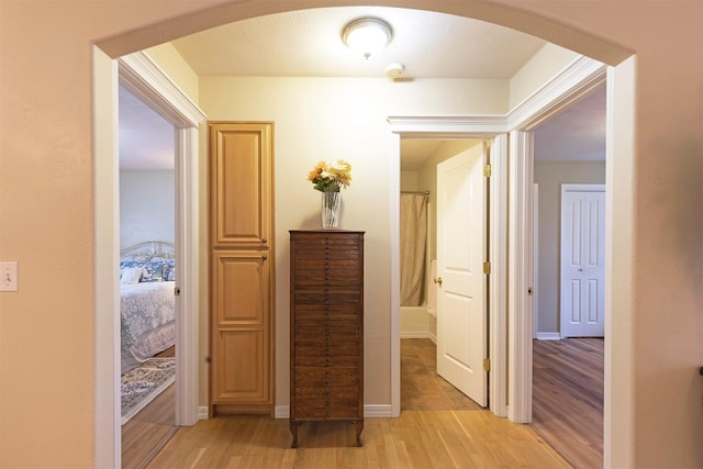 corridor featuring light wood-style flooring, arched walkways, and baseboards