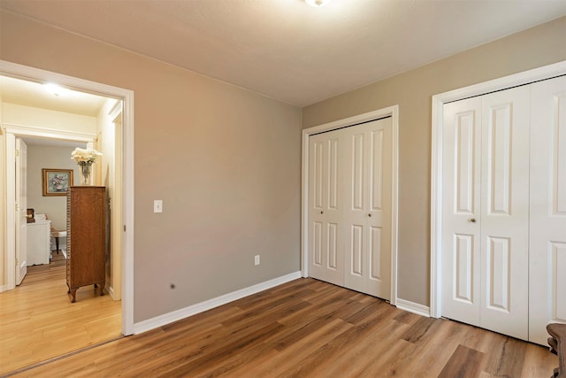 bedroom with baseboards, light wood finished floors, and two closets