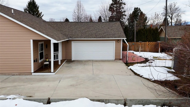 snow covered garage featuring fence and concrete driveway