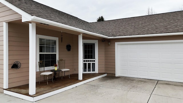 entrance to property featuring a garage, concrete driveway, and roof with shingles