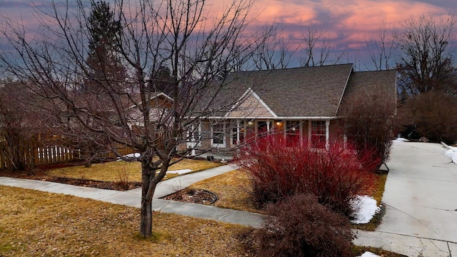 view of front of house with roof with shingles, fence, and a lawn