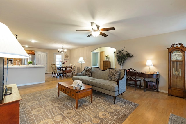 living room with arched walkways, light wood-style flooring, baseboards, and ceiling fan with notable chandelier