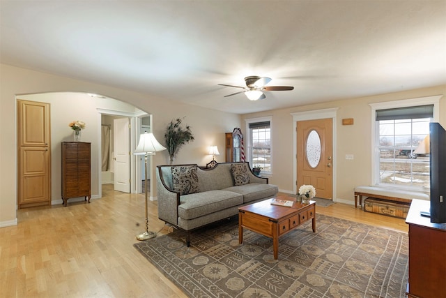 living room featuring arched walkways, ceiling fan, light wood-style flooring, and baseboards