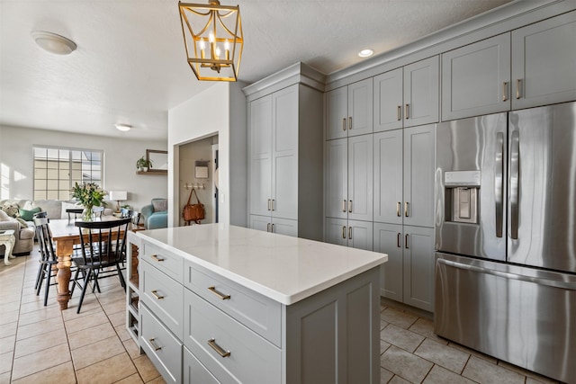 kitchen with light countertops, gray cabinetry, open floor plan, light tile patterned flooring, and stainless steel fridge