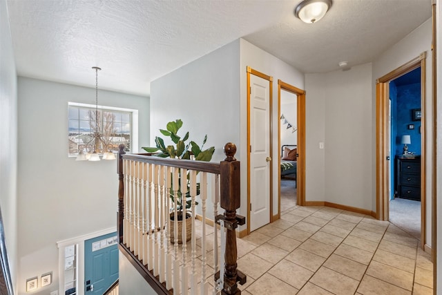 corridor featuring a textured ceiling, light tile patterned floors, a notable chandelier, an upstairs landing, and baseboards