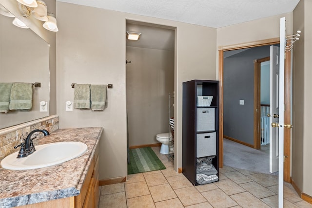 bathroom with a textured ceiling, toilet, vanity, baseboards, and tile patterned floors