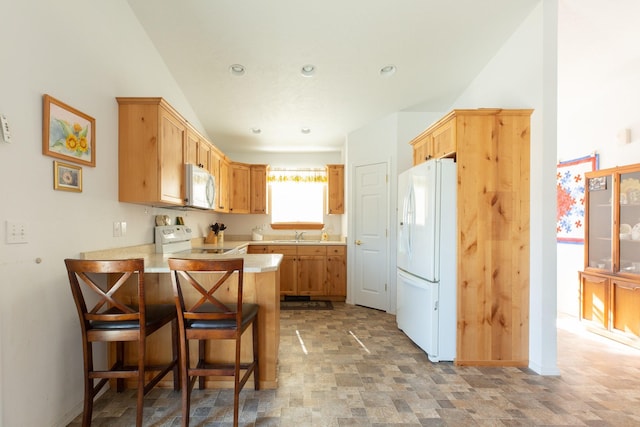 kitchen featuring a peninsula, white appliances, a breakfast bar, a sink, and light countertops