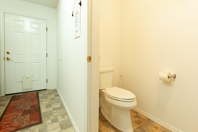 bathroom featuring toilet, stone finish flooring, and baseboards