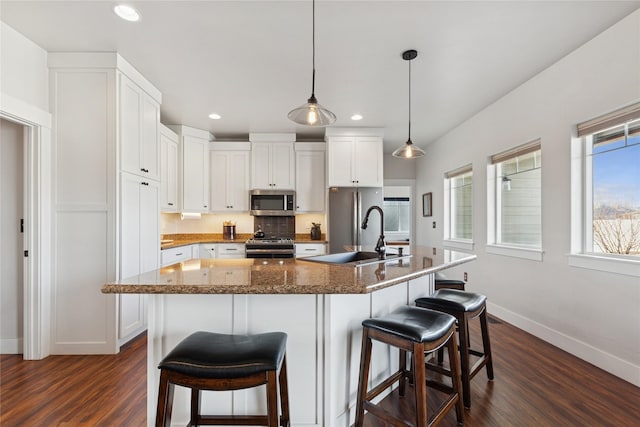 kitchen with stainless steel appliances, dark wood-type flooring, white cabinets, a sink, and baseboards