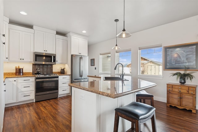 kitchen with appliances with stainless steel finishes, dark wood-type flooring, a sink, and light stone countertops