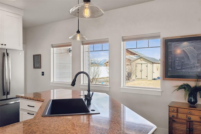 kitchen with stone countertops, a sink, white cabinetry, hanging light fixtures, and freestanding refrigerator