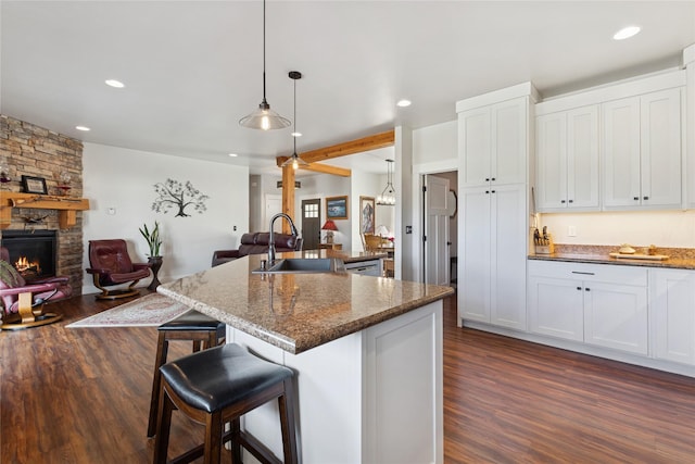 kitchen featuring a stone fireplace, a sink, open floor plan, dark wood-style floors, and a kitchen bar