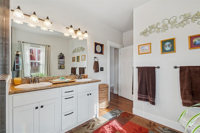 bathroom featuring wood finished floors, a sink, baseboards, and double vanity