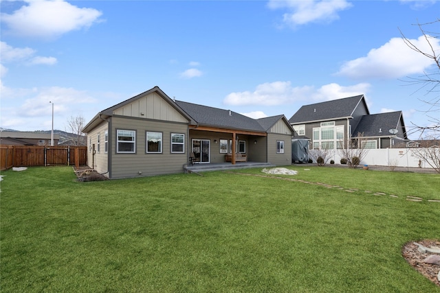 rear view of house with a yard, board and batten siding, a patio, and a fenced backyard