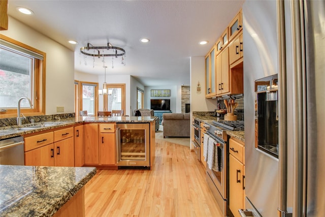 kitchen with beverage cooler, glass insert cabinets, appliances with stainless steel finishes, a peninsula, and light wood-style floors