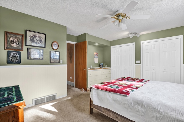 bedroom with a textured ceiling, ceiling fan, carpet flooring, visible vents, and multiple closets