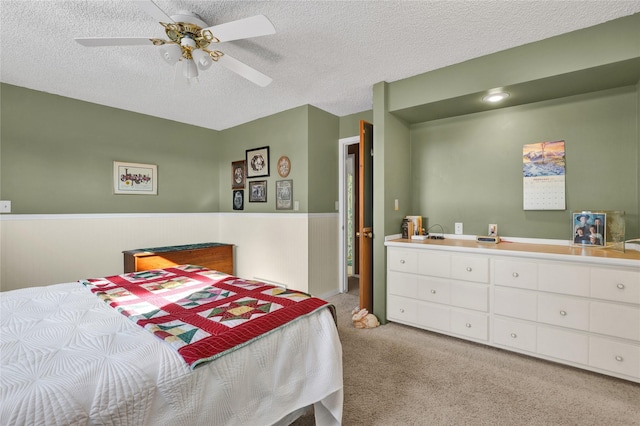 carpeted bedroom with a wainscoted wall, a textured ceiling, and a ceiling fan