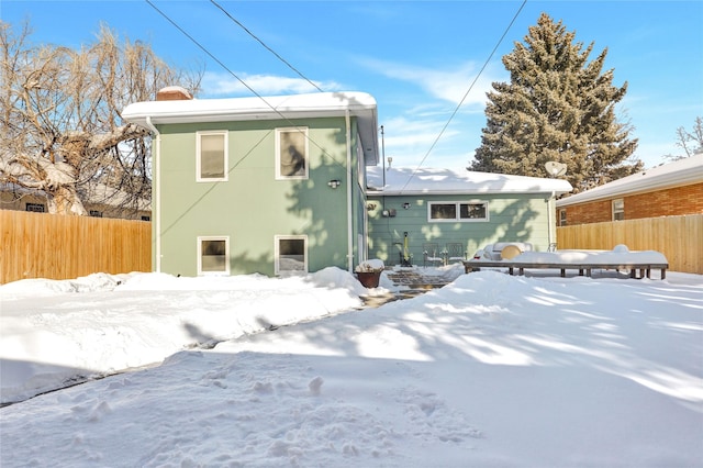 snow covered rear of property featuring fence