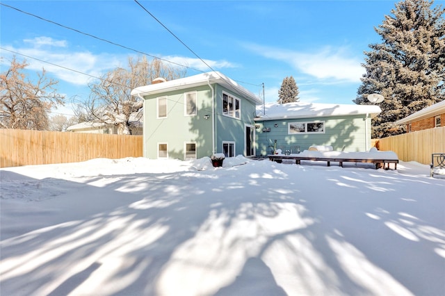 snow covered rear of property with fence, a wooden deck, and stucco siding