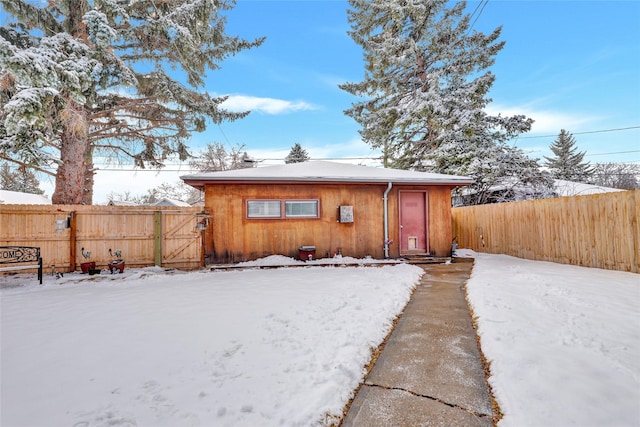 snow covered back of property with a gate and fence