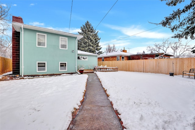 snow covered property with fence, a chimney, and stucco siding