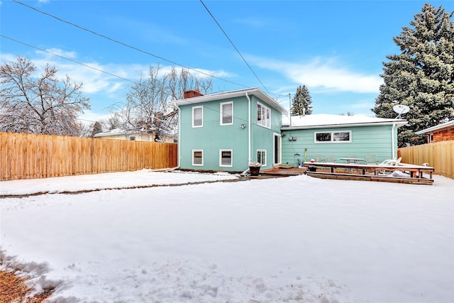 snow covered rear of property featuring a chimney, fence, a deck, and stucco siding