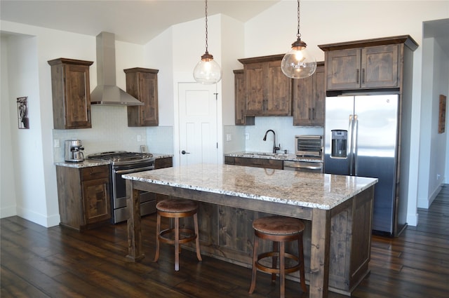 kitchen featuring dark brown cabinetry, a sink, a kitchen island, appliances with stainless steel finishes, and wall chimney range hood