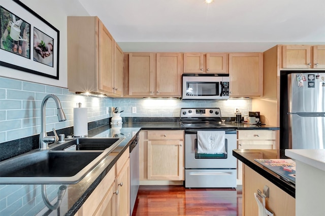 kitchen with light brown cabinets, a sink, appliances with stainless steel finishes, decorative backsplash, and dark countertops