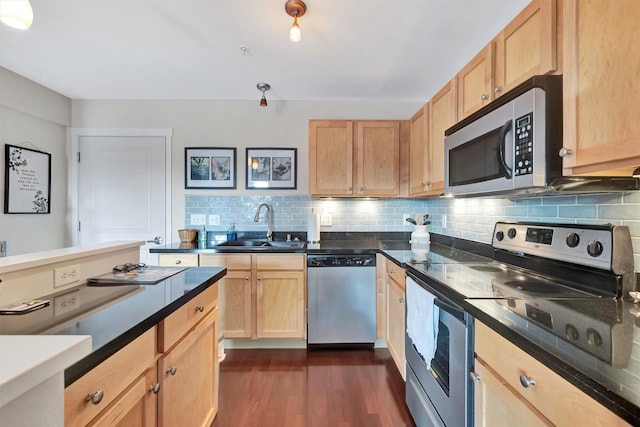 kitchen with a sink, appliances with stainless steel finishes, tasteful backsplash, dark countertops, and dark wood finished floors