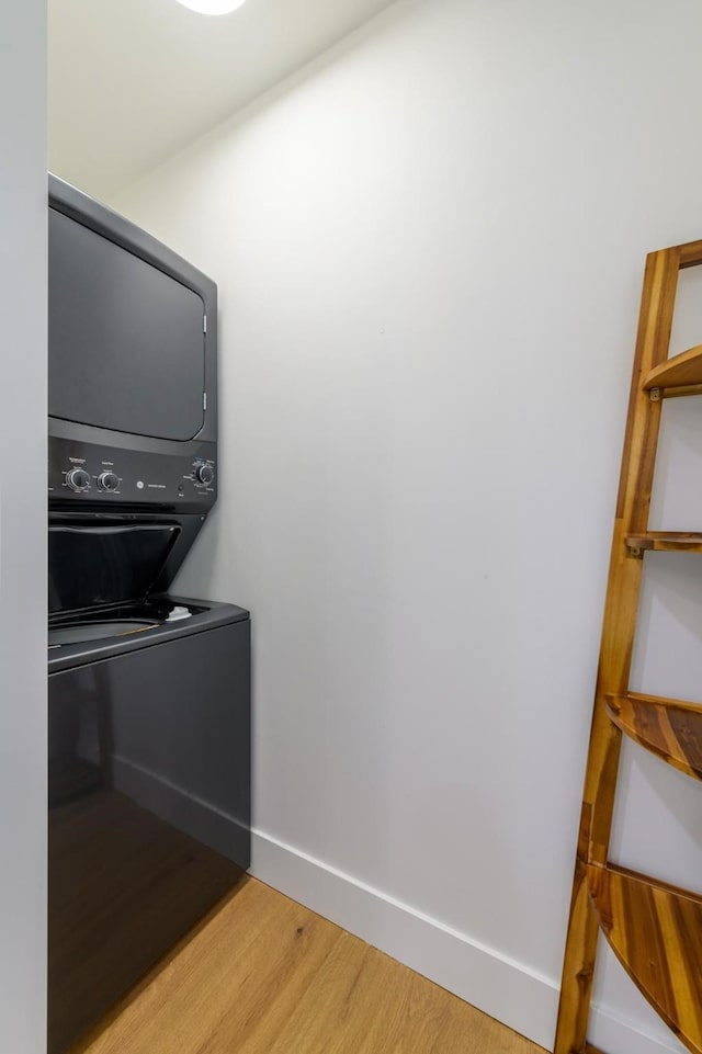 washroom with laundry area, light wood-type flooring, stacked washer / drying machine, and baseboards