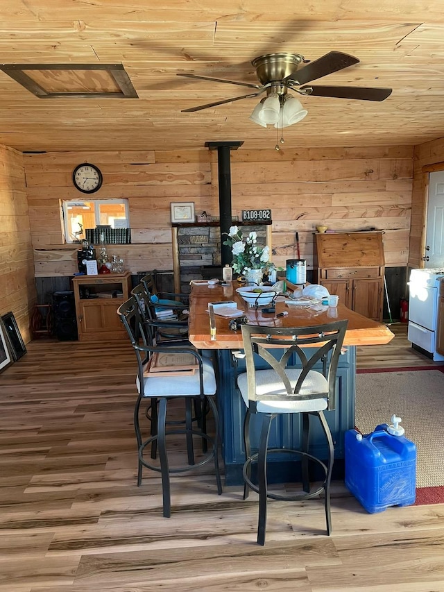 dining space with wooden ceiling, wood finished floors, a wood stove, and wooden walls