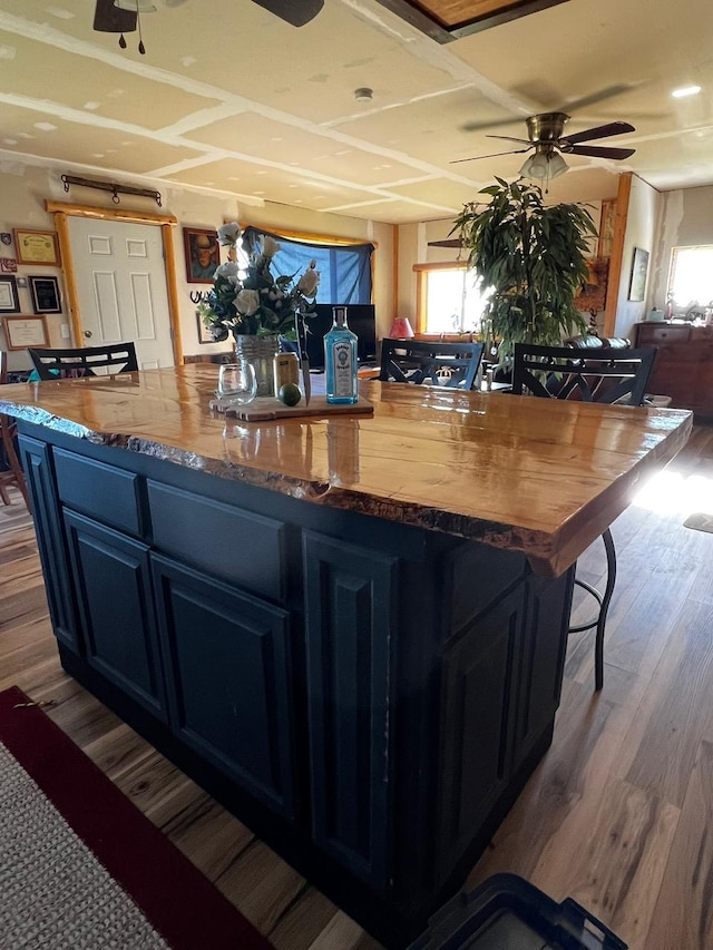 kitchen featuring a ceiling fan, butcher block counters, a kitchen island, a kitchen breakfast bar, and wood finished floors