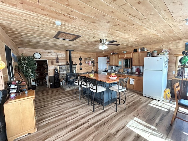 unfurnished dining area with wooden ceiling, a wood stove, wooden walls, and light wood-style flooring