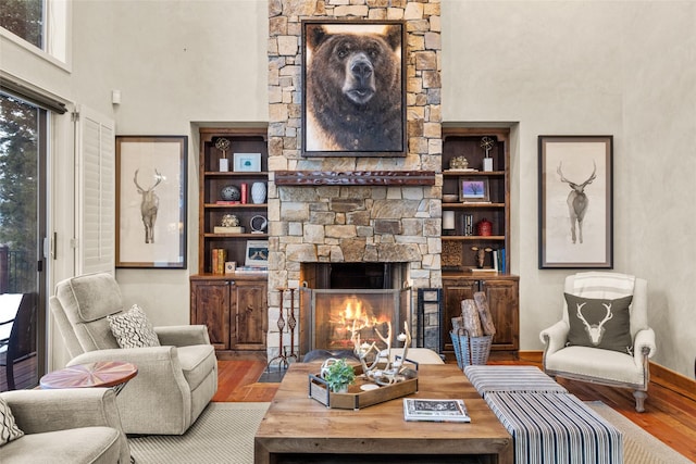 living area featuring a stone fireplace, wood finished floors, a towering ceiling, and baseboards