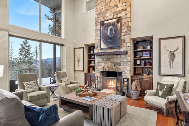 living area featuring built in shelves, a stone fireplace, a high ceiling, and wood finished floors