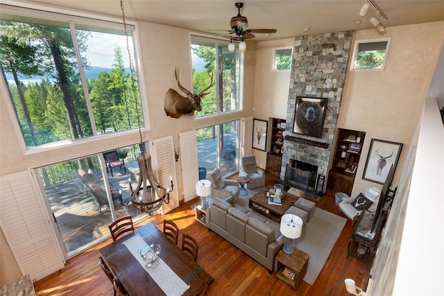 living room featuring a ceiling fan, wood finished floors, rail lighting, a high ceiling, and a stone fireplace