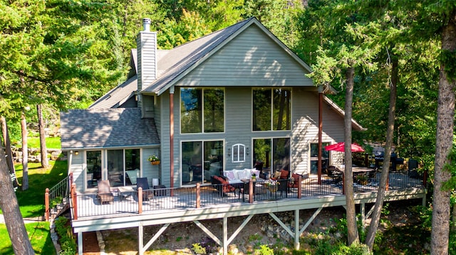 back of property with a shingled roof, a chimney, outdoor lounge area, and a wooden deck