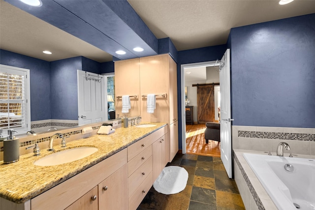 full bath featuring double vanity, a sink, stone tile floors, and a bath