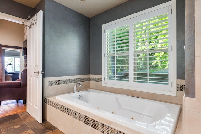 ensuite bathroom featuring stone tile flooring, a tub with jets, and connected bathroom