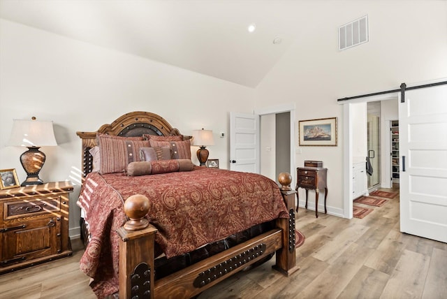 bedroom with light wood finished floors, a barn door, visible vents, and high vaulted ceiling