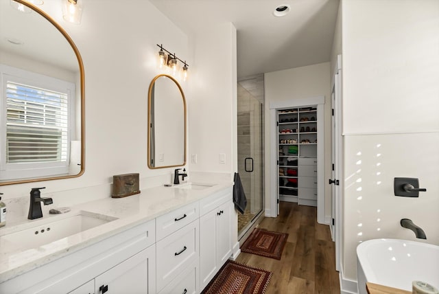 full bathroom with double vanity, wood finished floors, a stall shower, and a sink