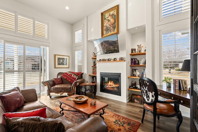 living area with built in features, recessed lighting, a high ceiling, a glass covered fireplace, and wood finished floors